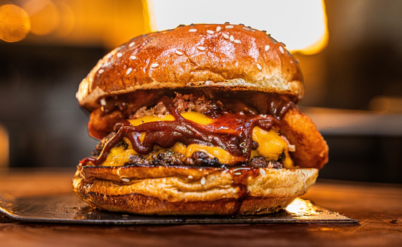 Nahaufnahme eines saftigen Burgers mit Käse, Zwiebelringen und BBQ-Sauce © Shutterstock / edulauton