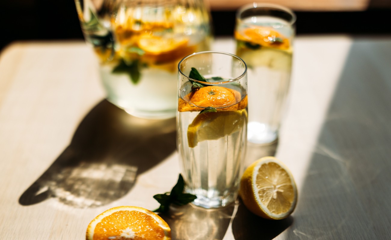 Zwei Gläser mit Wasser und Zitrusfrüchten auf einem Tisch bei Sonnenlicht © Shutterstock / ShvedKris