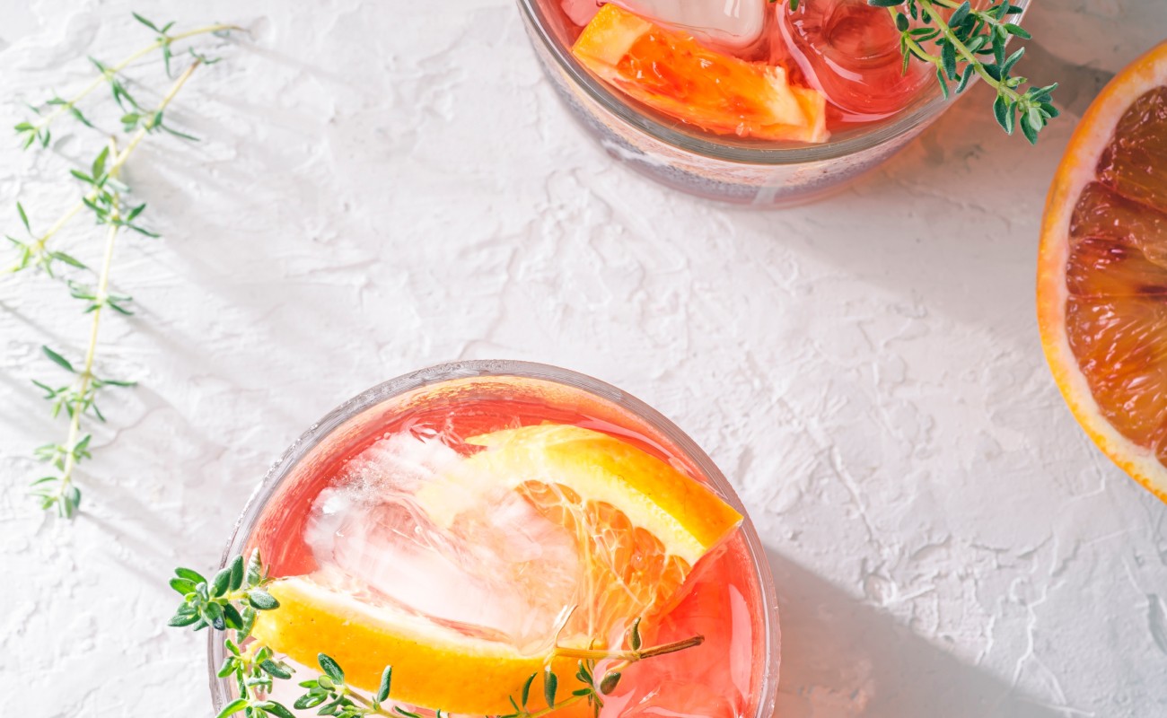 Zwei Gläser roter Cocktail mit Eis, Orangenscheiben und Thymian auf hellem Untergrund © Shutterstock / UlliAb