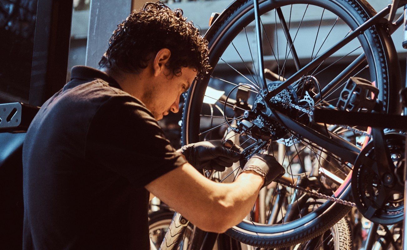 Mann repariert ein Fahrrad in einer Werkstatt voller Fahrräder © Shutterstock / FXQuadro